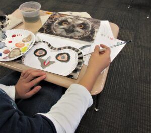 a student, mostly off screen is painting an owl from a photo of an owl.