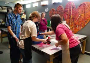 five students stand around a printmaking station adding hearts to an image