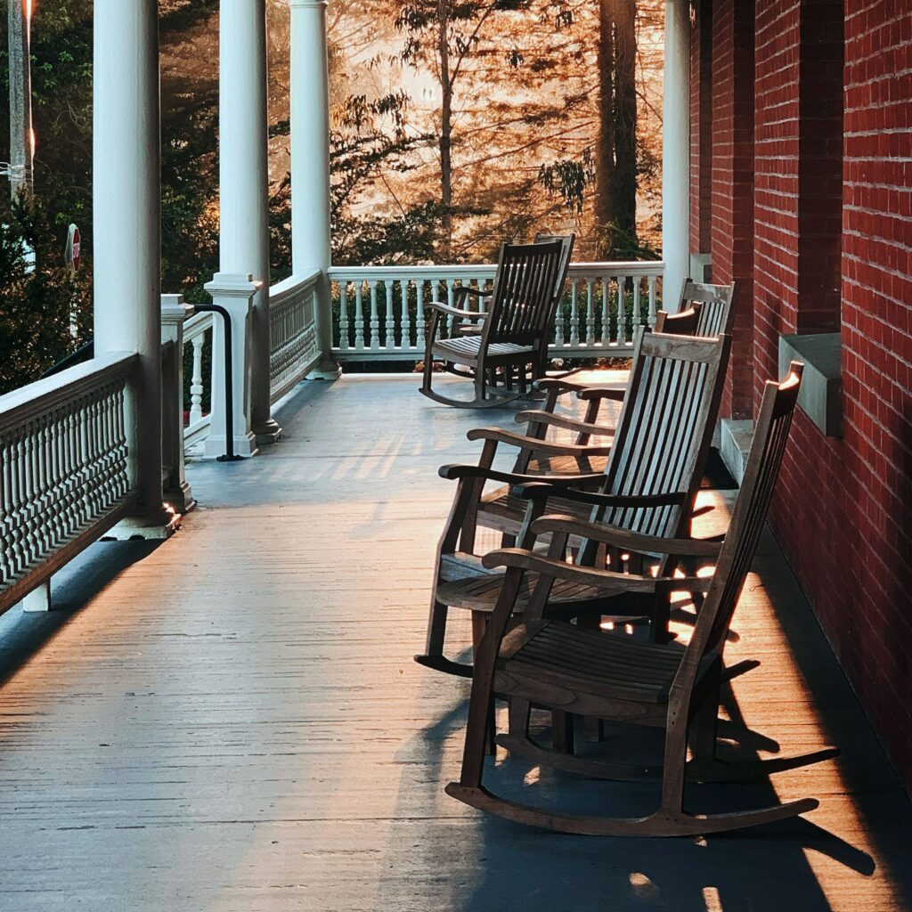 Empty wooden rocking chairs on a covered porch in late afternoon sunlight.